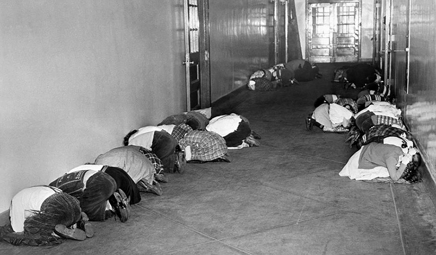 Black and white photograph of a hallway at an elementary school in Baltimore, Maryland. Children are lined up along the walls in the tuck and duck position. 