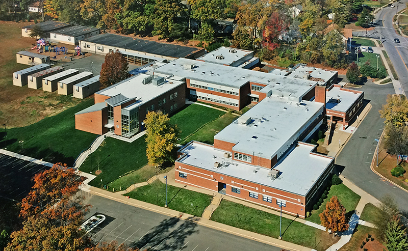 Color aerial photograph of Crestwood Elementary School taken from a drone hovering above Hanover Avenue. The school is pictured from the southeast at an angle. Visible are the new classroom wing, the six trailers along the blacktop, and the large modular classrooms behind the school. 