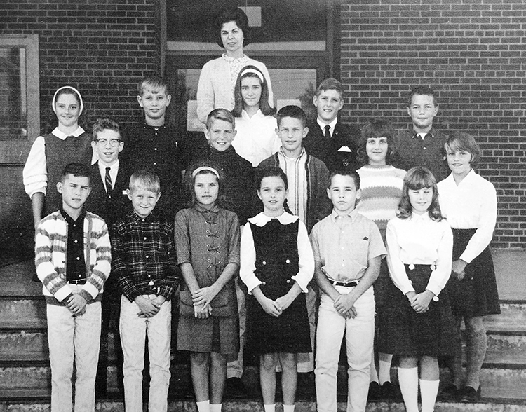 Black and white yearbook photograph of Crestwood's S.C.A. Executive Committee taken in 1966. The children are arranged in three rows on the steps in front of the school. 16 children are pictured, and even mix of boys and girls. The boys are wearing button down shirts or sweaters, and slacks. The girls are wearing dresses or skirts, and ankle or knee socks. A teacher sponsor stands behind them. 